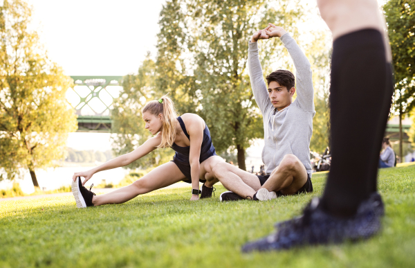 Young runners in nature warming up and stretching arms and legs.