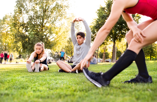 Group of young runners in nature warming up and stretching arms and legs.