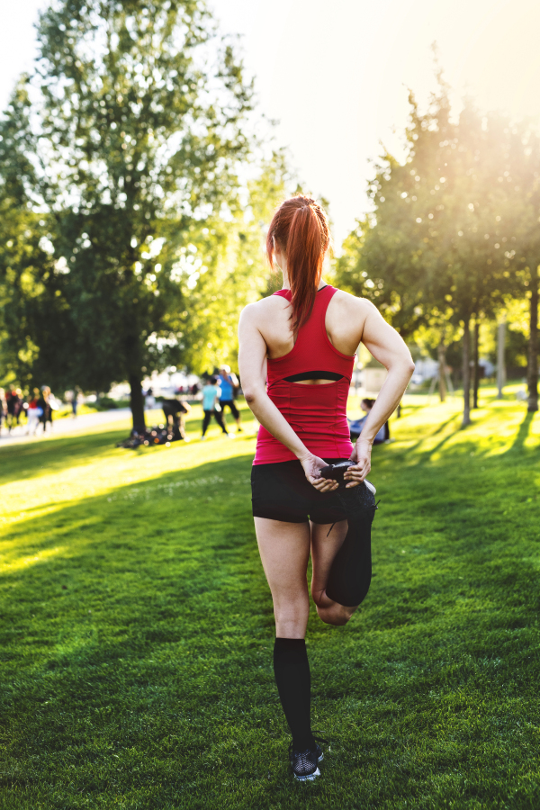 Beautiful young runner in nature warming up and stretching legs. Rear view.