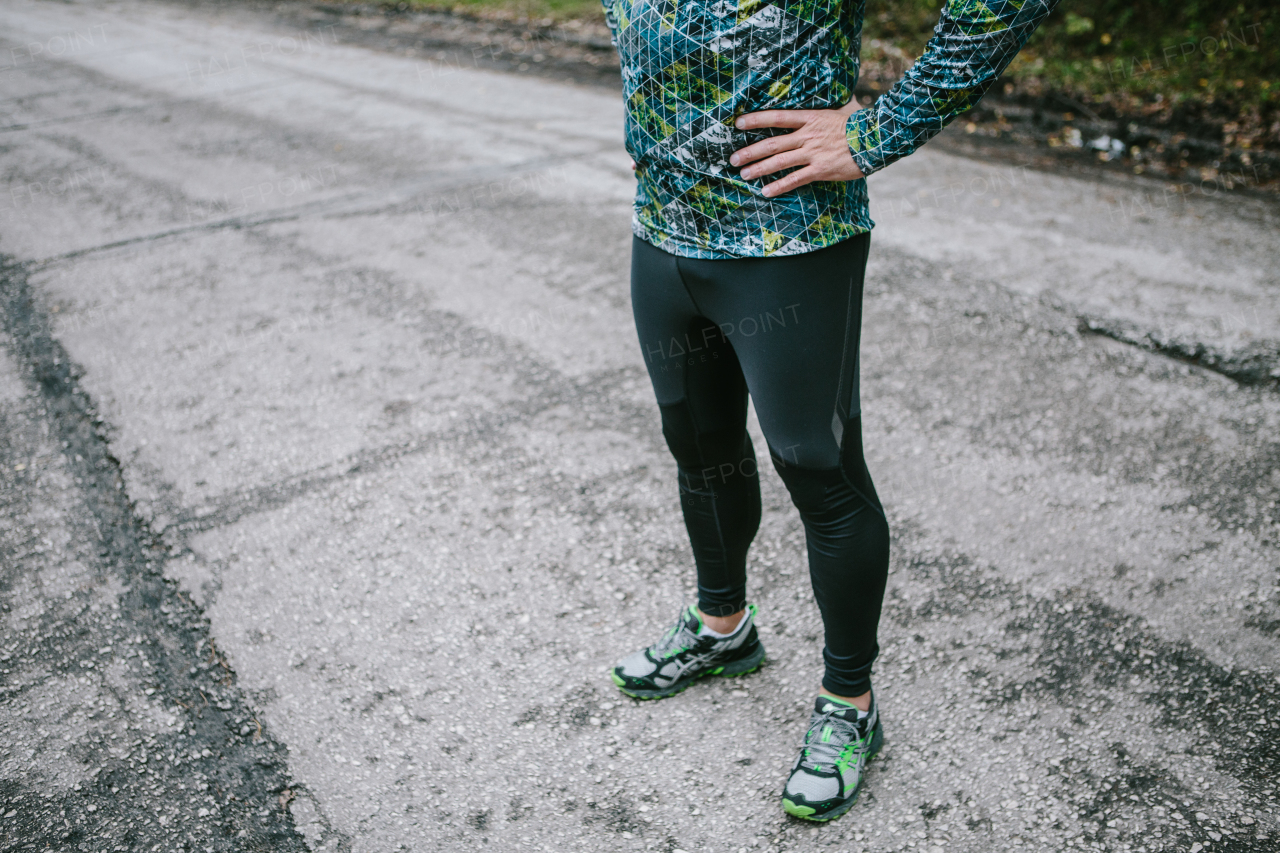 Lower body of fit runner with his hands on hips against old gray road