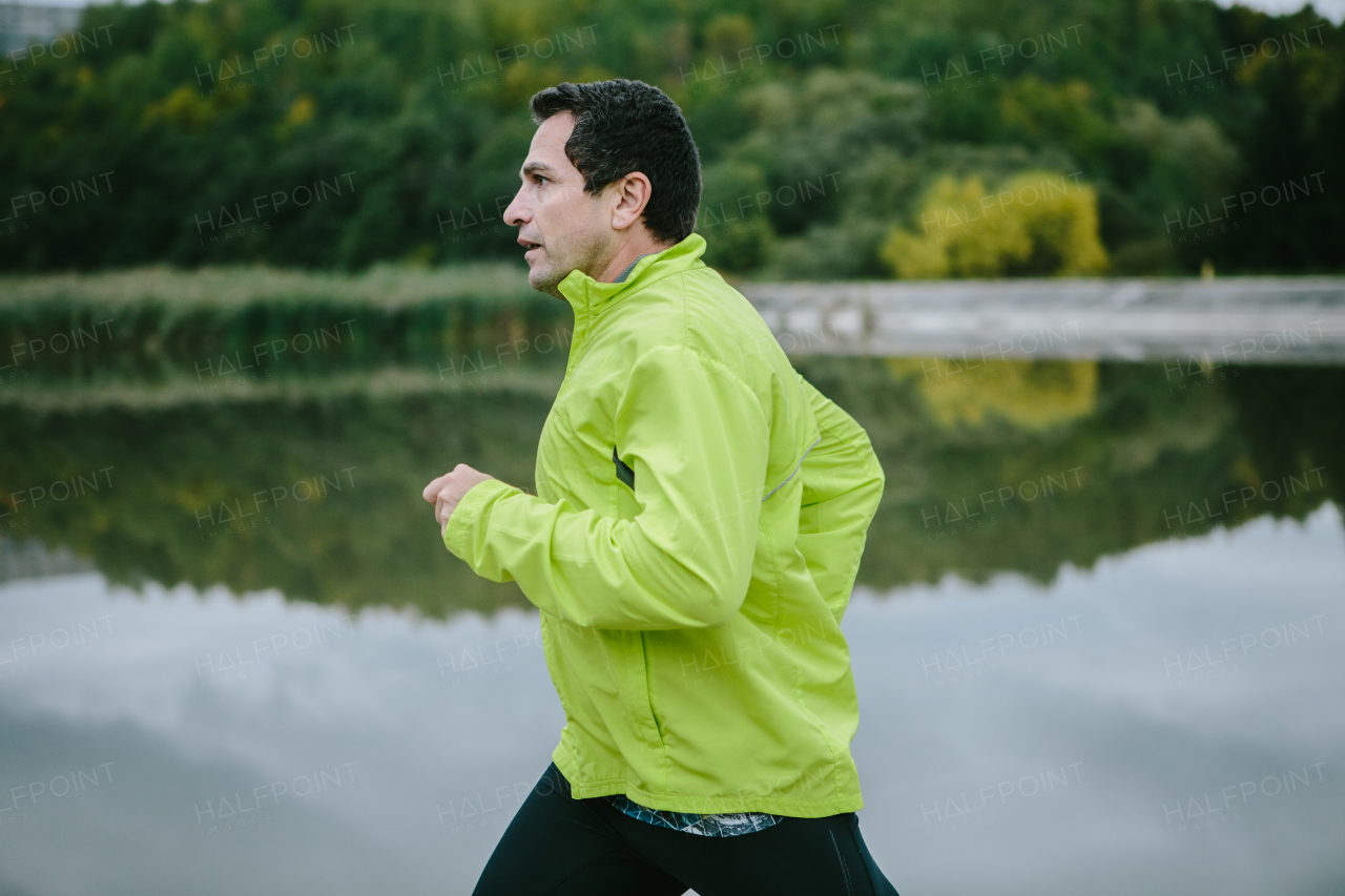 Man in yellow neon jacket runnig at the lake . Water reflecting nature.