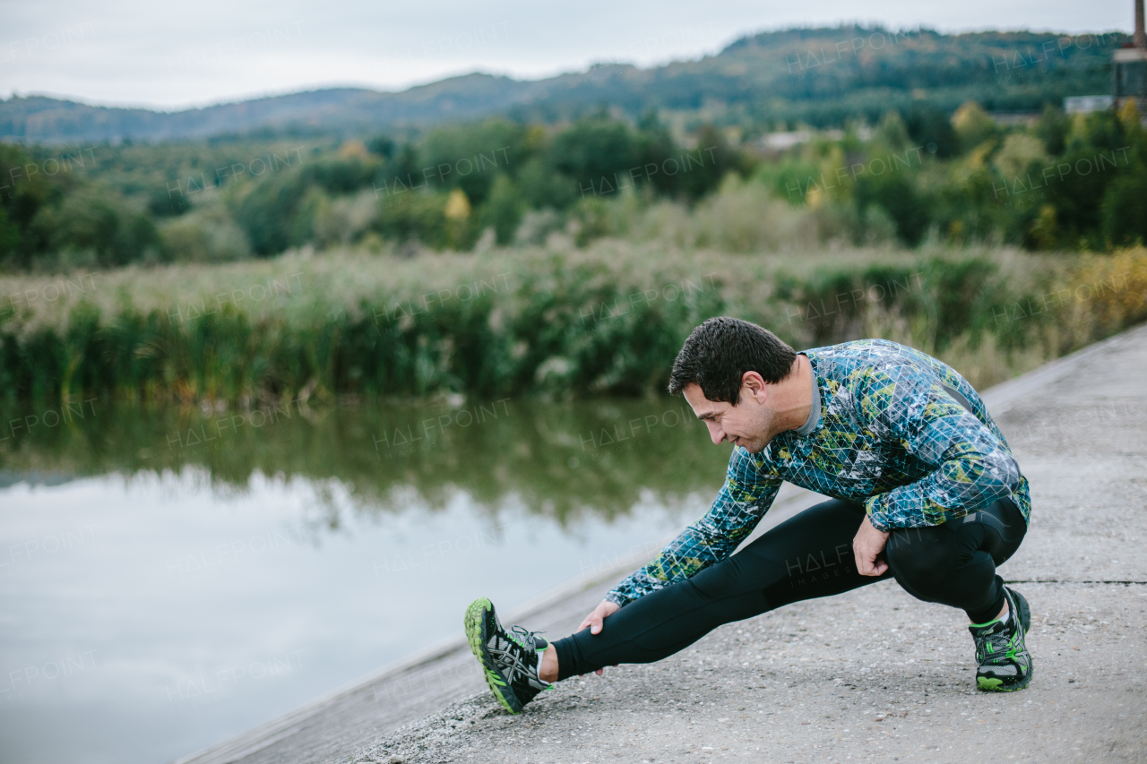 Runner on the path at the lake warming up and stretching against green nature