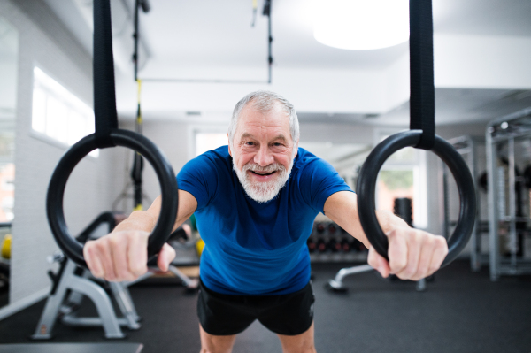 Senior man in sports clothing in gym working out on gymnastic rings. Close up of hands.