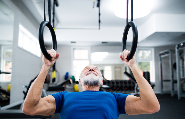 Senior man in sports clothing in gym working out on gymnastic rings.