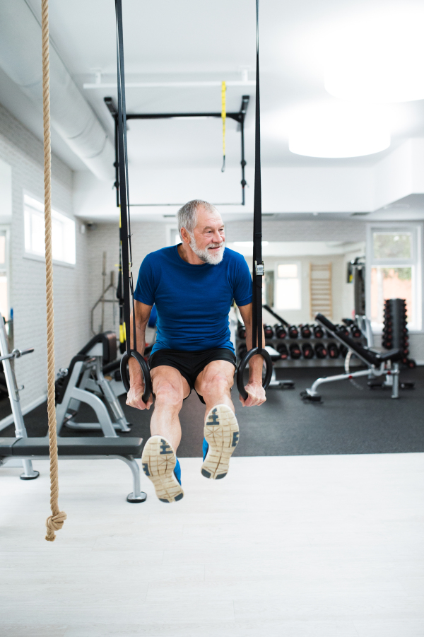 Senior man in sports clothing in gym working out on gymnastic rings.