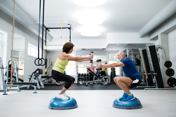 Beautiful fit senior couple in gym working out with weights and squatting at the same time