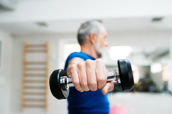 Senior man in sports clothing in gym working out with weights. Close up of hands.