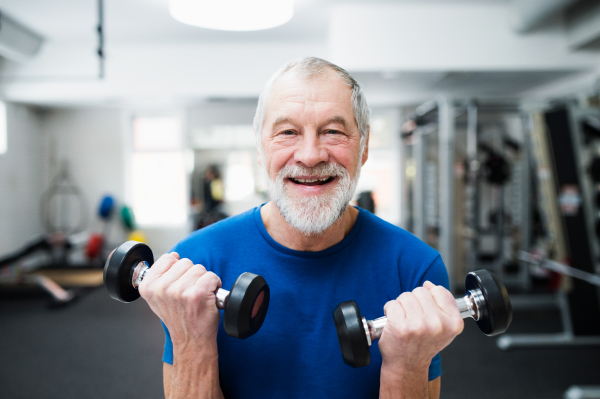 Senior man in sports clothing in gym working out with weights.