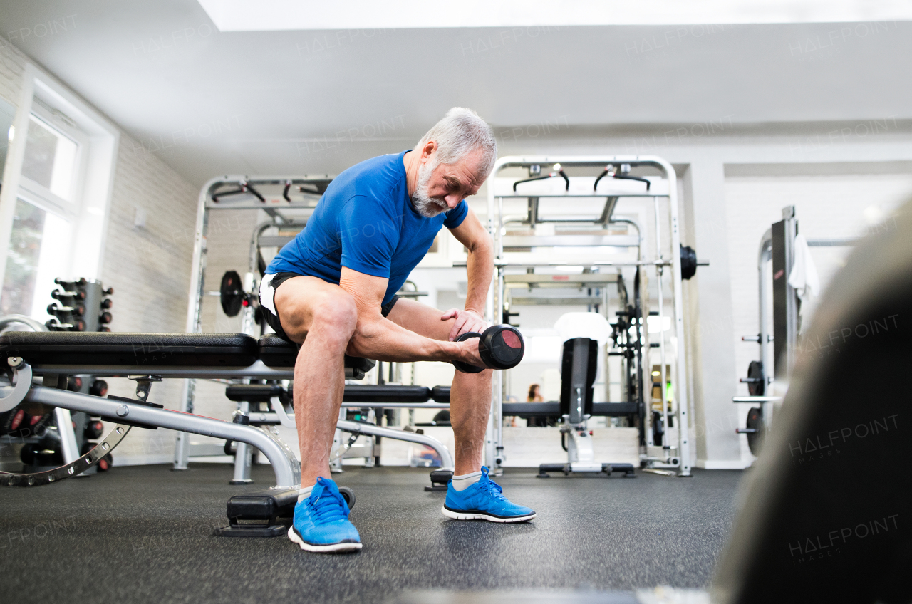 Senior man in sports clothing in gym working out with weights.