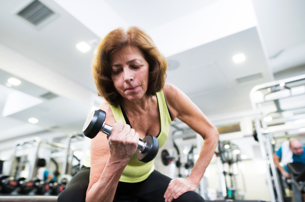 Senior woman in sports clothing in gym working out with weights. Close up of hands.