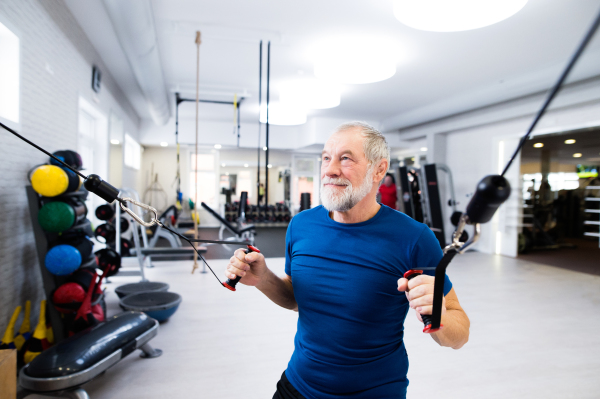 Fit senior man in sports clothing in gym working out with resistance bands.