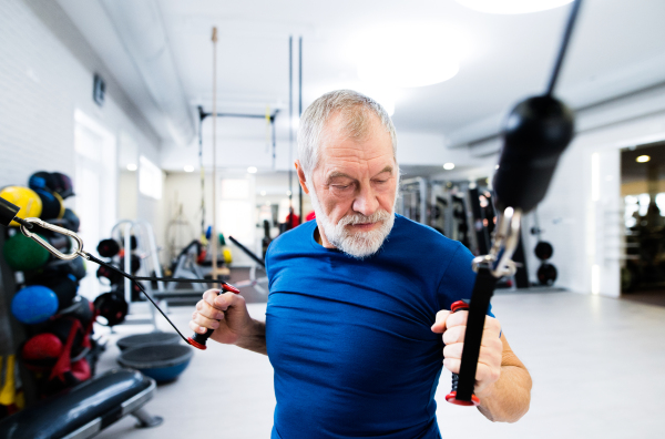 Fit senior man in sports clothing in gym working out with resistance bands.