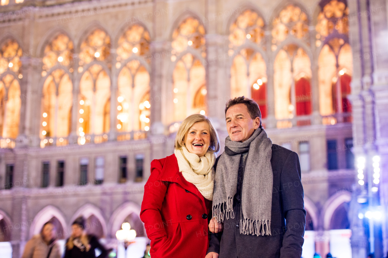 Senior couple in winter clothes on a walk in illuminated night city. Historical building. Vienna, Austria.