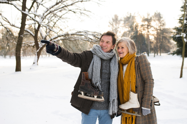 Beautiful senior woman and man in winter nature with ice skates going to outdoor rink.