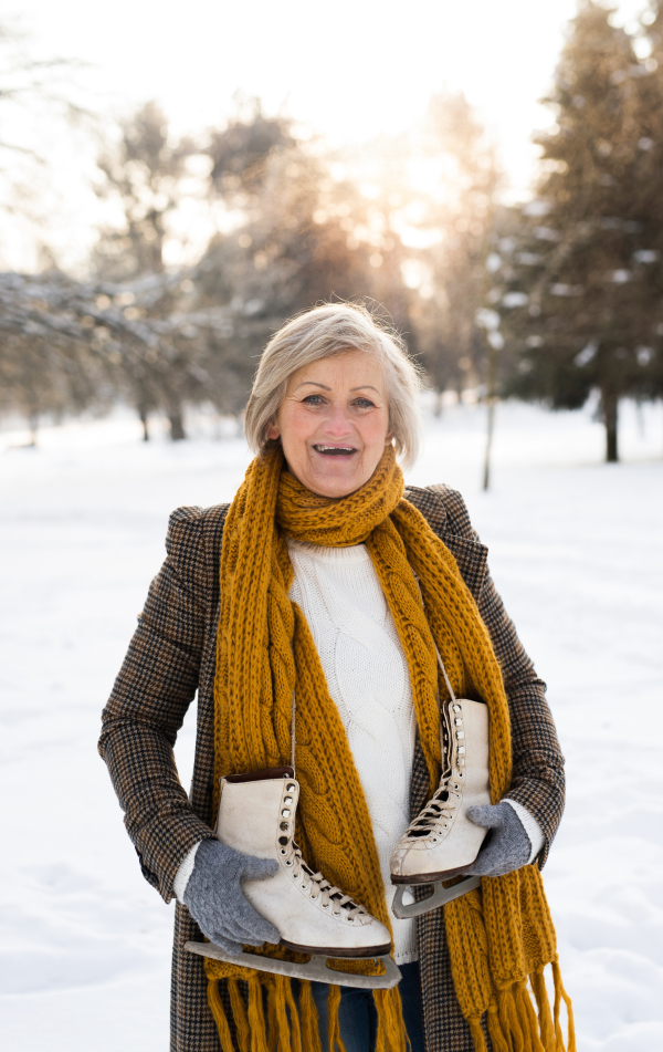 Beautiful senior woman in sunny winter nature going ice skating.