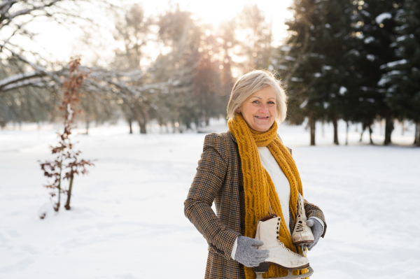 Beautiful senior woman in sunny winter nature going ice skating.