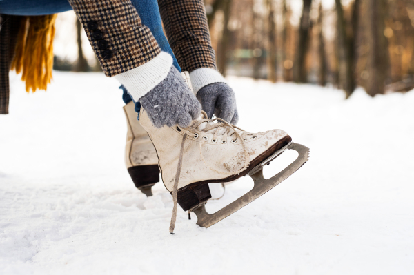 Unrecognizable woman in winter clothes putting on old ice skates. Close up. Snowy winter nature.