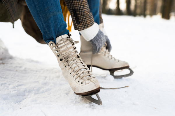 Unrecognizable woman in winter clothes putting on old ice skates. Close up. Snowy winter nature.