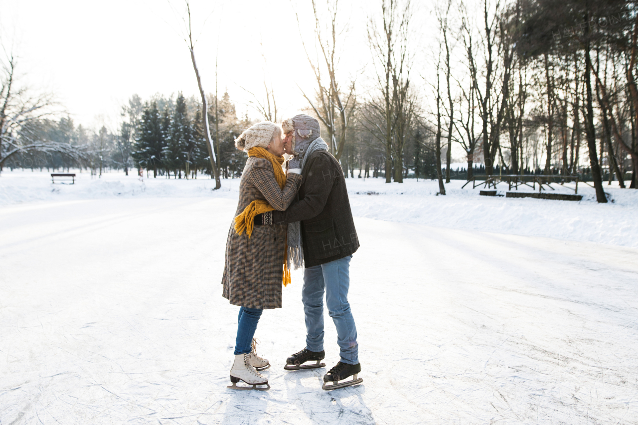 Beautiful senior woman and man in sunny winter nature ice skating. Married couple in park kissing.