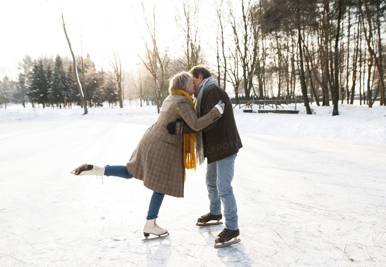 Beautiful senior woman and man in sunny winter nature ice skating, hugging and kissing.