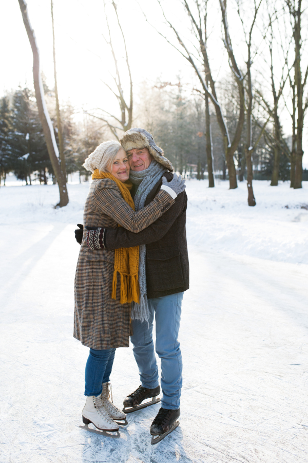 Beautiful senior woman and man in sunny winter nature ice skating, hugging.