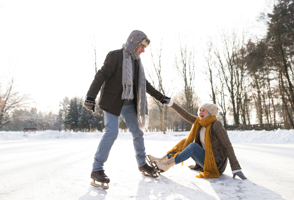 Beautiful senior couple in sunny winter nature ice skating, man helping woman to stand up.