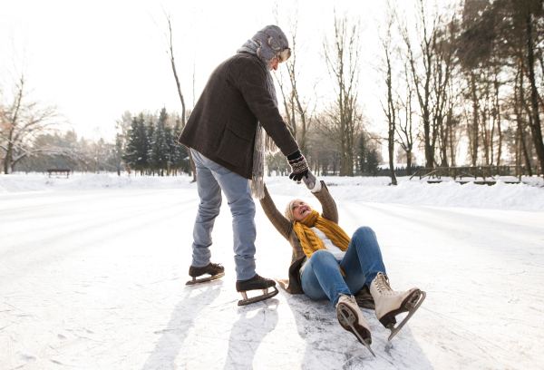 Beautiful senior couple in sunny winter nature ice skating, man helping woman to stand up.