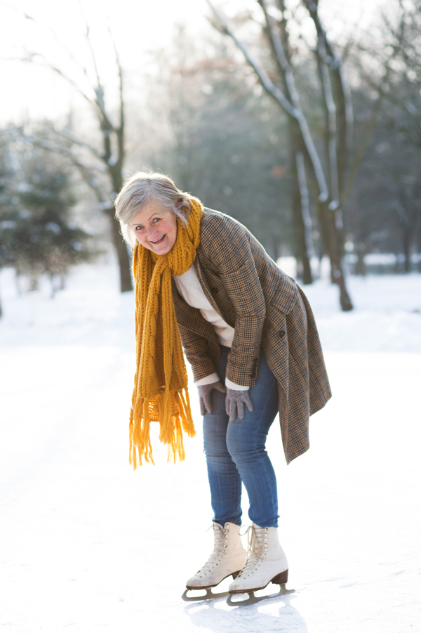 Beautiful senior woman in sunny winter nature ice skating.