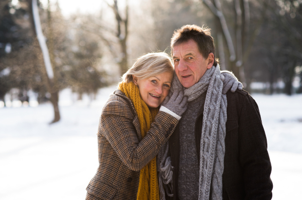 Beautiful senior woman and man in sunny winter nature ice skating, hugging.