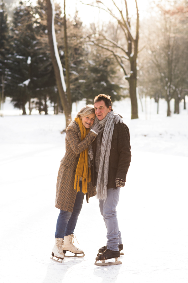 Beautiful senior woman and man in sunny winter nature ice skating, hugging.