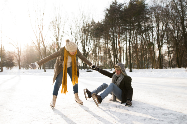 Beautiful senior couple in sunny winter nature ice skating, woman helping man to stand up.