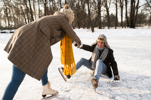 Beautiful senior couple in sunny winter nature ice skating, woman helping man to stand up.