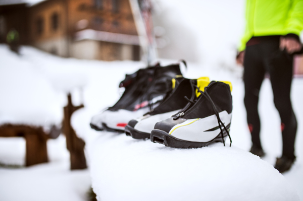 Unrecognizable active senior couple getting ready for cross-country skiing. Ski boots on a snow covered bench. Winter time.