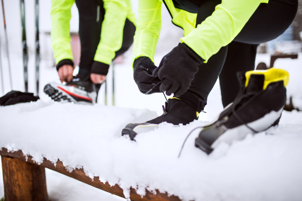 Active senior couple getting ready for cross-country skiing. Unrecognizable man and woman putting on ski boots. Winter time.