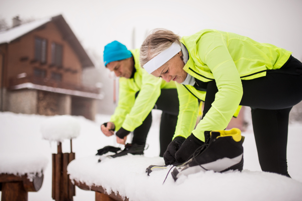 Active senior couple getting ready for cross-country skiing. A man and woman putting on ski boots. Winter time.