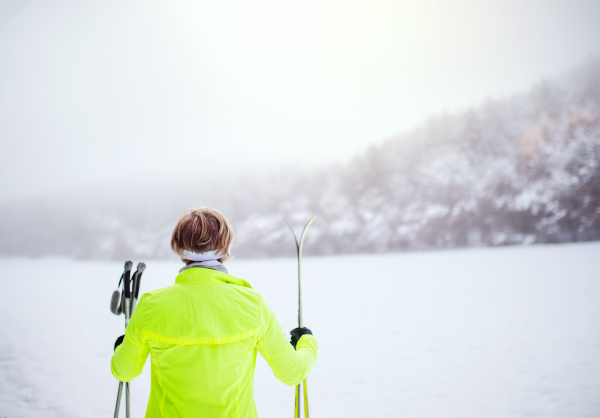 Active senior woman going cross-country skiing. Winter time. Rear view.