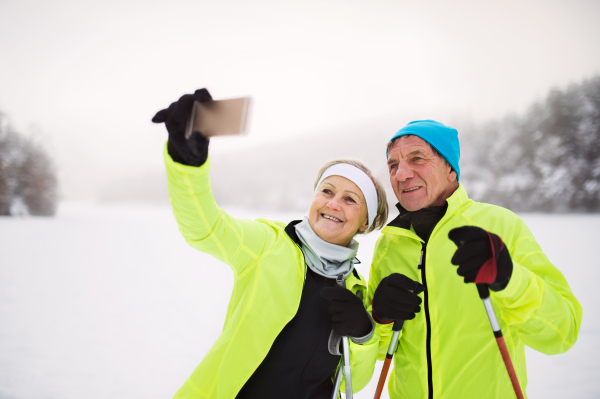 Senior couple cross-country skiing. An active man and woman taking a selfie with a smartphone. Winter time.