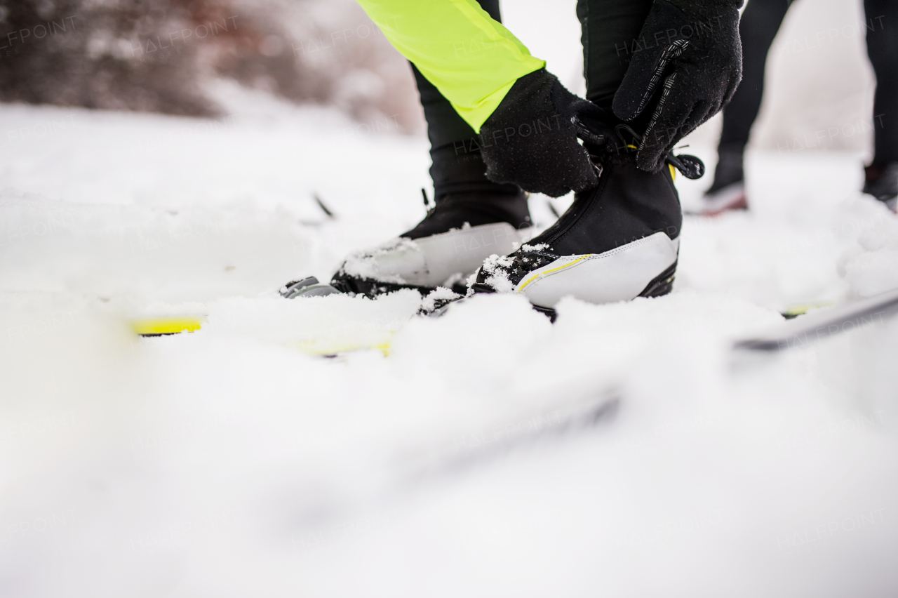 Active senior couple getting ready for cross-country skiing. Unrecognizable man and woman putting on ski boots. Winter time.