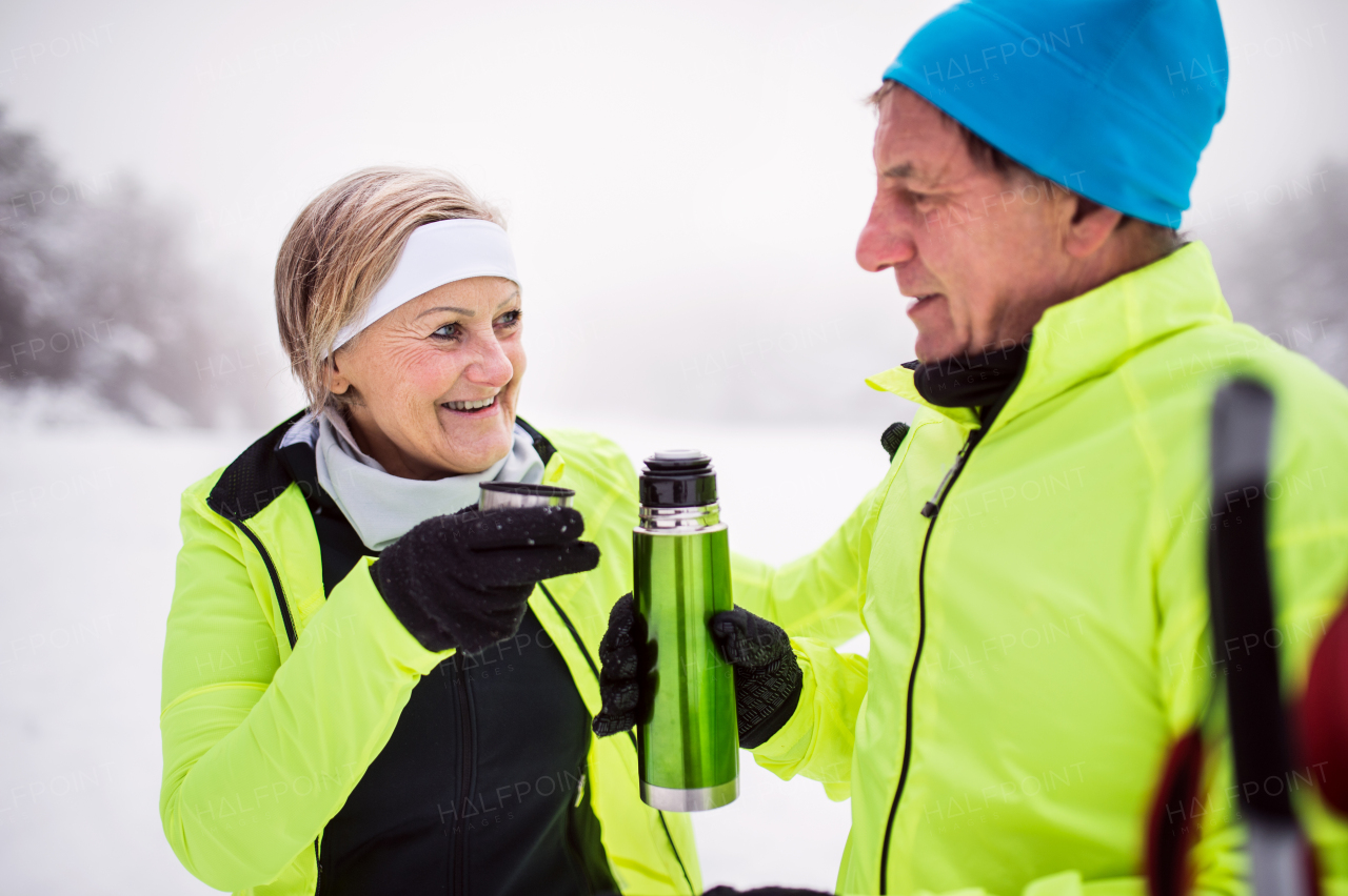 Active senior couple cross-country skiing. A man and woman drinking hot tea. Winter time.