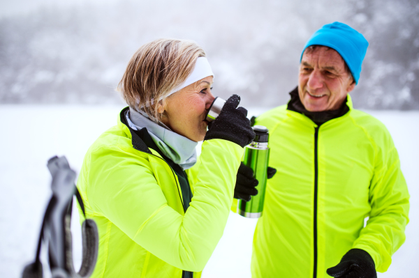 Active senior couple cross-country skiing. A man and woman drinking hot tea. Winter time.