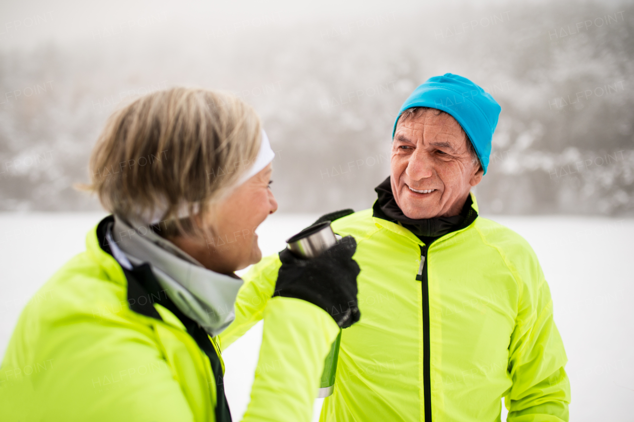 Active senior couple cross-country skiing. A man and woman drinking hot tea. Winter time.