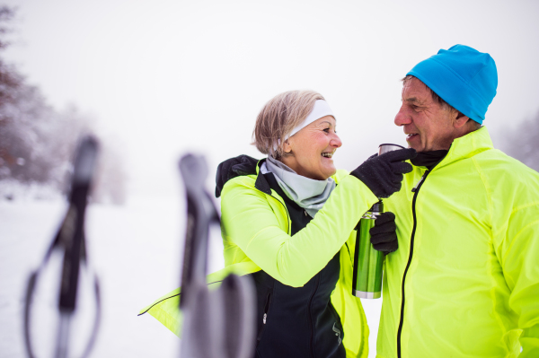 Active senior couple cross-country skiing. A man and woman drinking hot tea. Winter time.