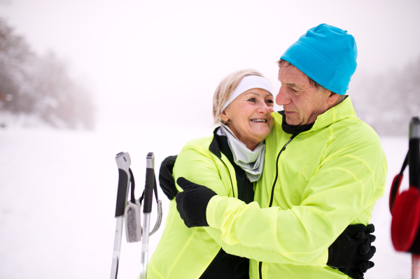 Active senior couple cross-country skiing, hugging. Winter time.