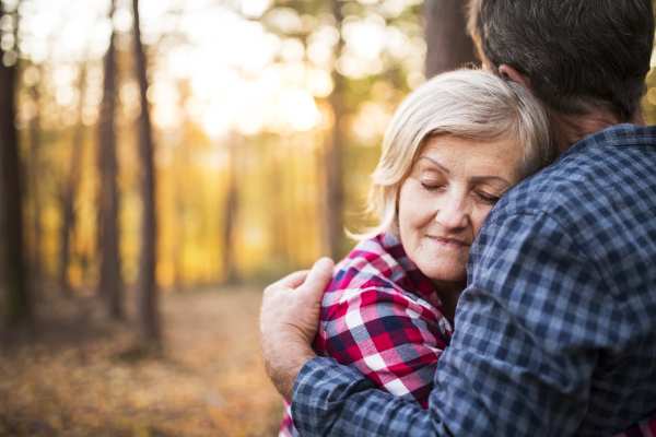 Active senior couple on a walk in a beautiful autumn forest. Unrecognizable man and woman hugging, eyes closed.