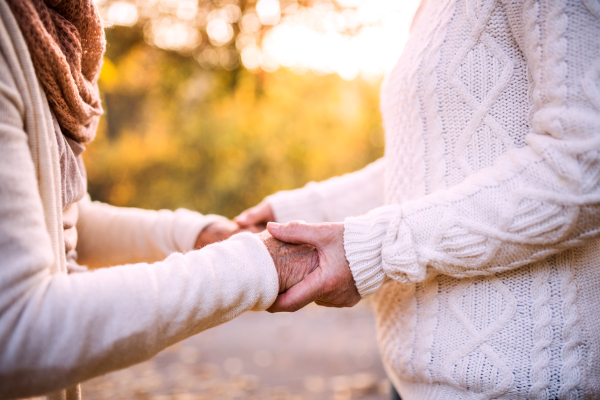 Unrecognizable senior women on a walk in autumn nature. Senior woman holding hands of her elderly mother.