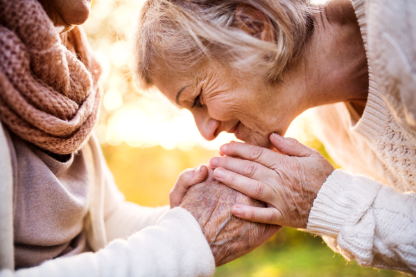 Unrecognizable senior women on a walk in autumn nature. Senior woman holding hands of her elderly mother.