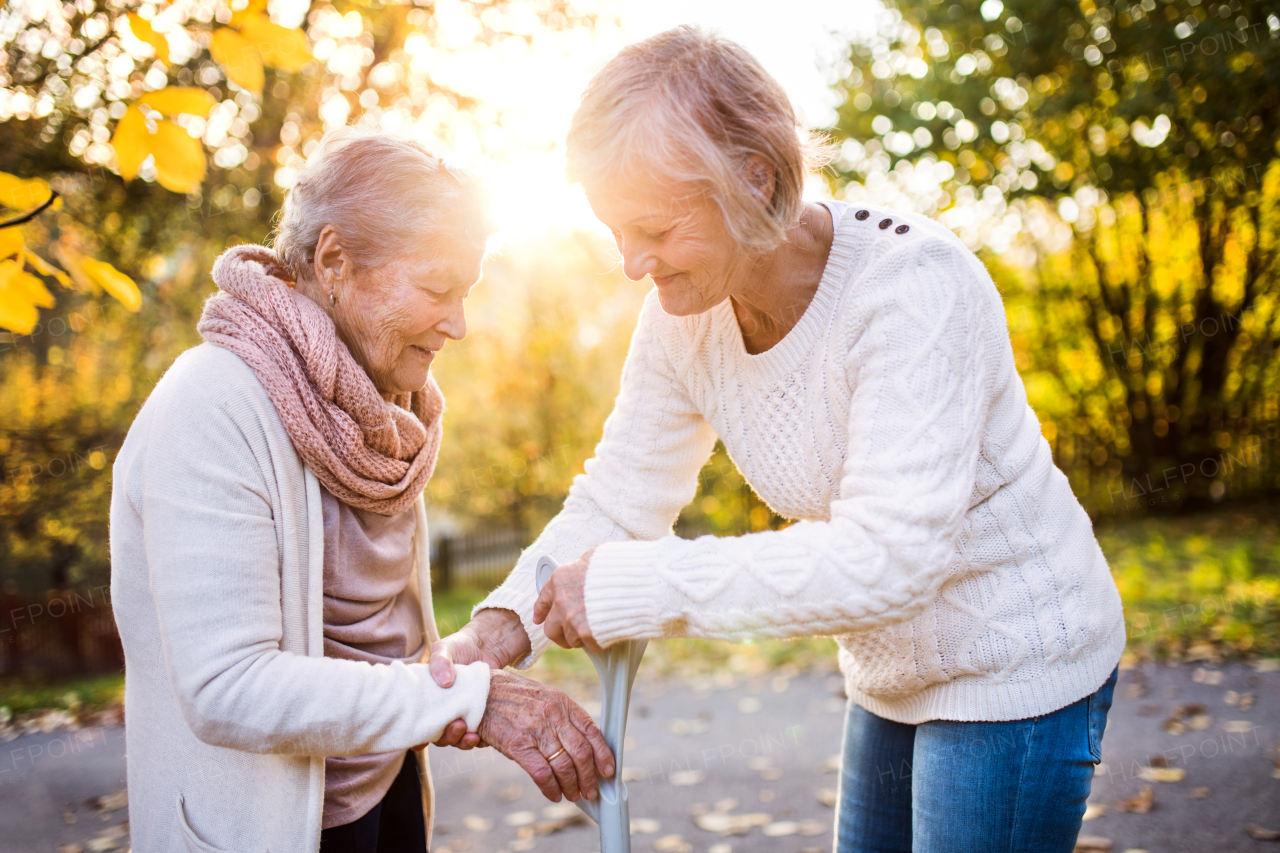 Senior women on a walk in autumn nature. An elderly woman with crutch and her senior daughter walking outside.