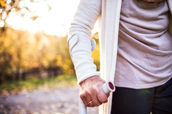 Unrecognizable elderly woman with a crutch in autumn nature. Senior woman on a walk.