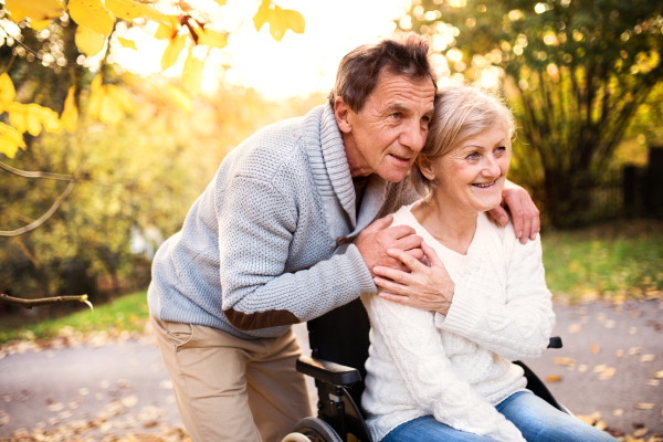 Senior couple in autumn nature. Man and woman in a wheelchair on a walk.