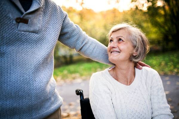 Senior couple in autumn nature. Man and woman in a wheelchair on a walk.